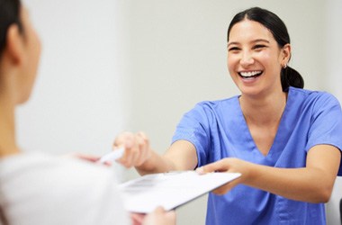 Dental assistant smiling while handing patient form